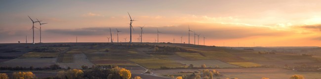 Wind plant over fields with a sunset behind it