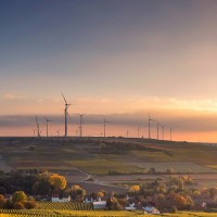 wind turbines behind a farm with a sunset